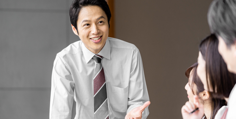 会議中に笑顔で話すビジネスマンと3名の社員