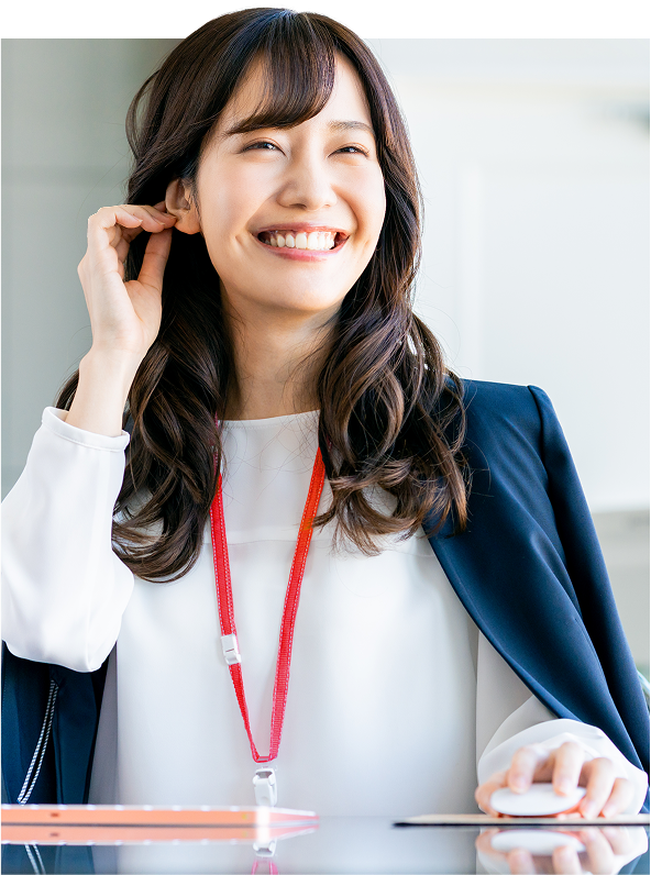 笑顔でオフィスのデスクに座る女性 赤いファイルを手に持ち、横を向いて微笑む男性